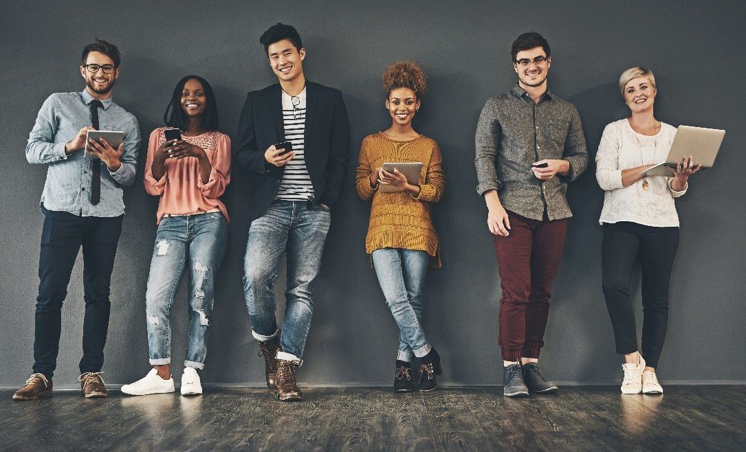Group of diverse young people leaning against a grey wall