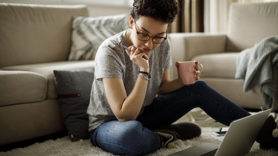 Young Woman working from home who is sitting on the floor in front of the couch.