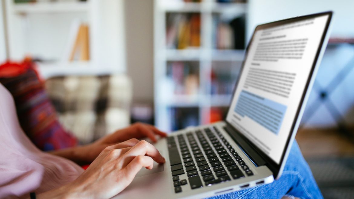 Close up image of a young woman working at home, typing on the keyboard, reading or editing text, laid back relaxed on the sofa in the living room.