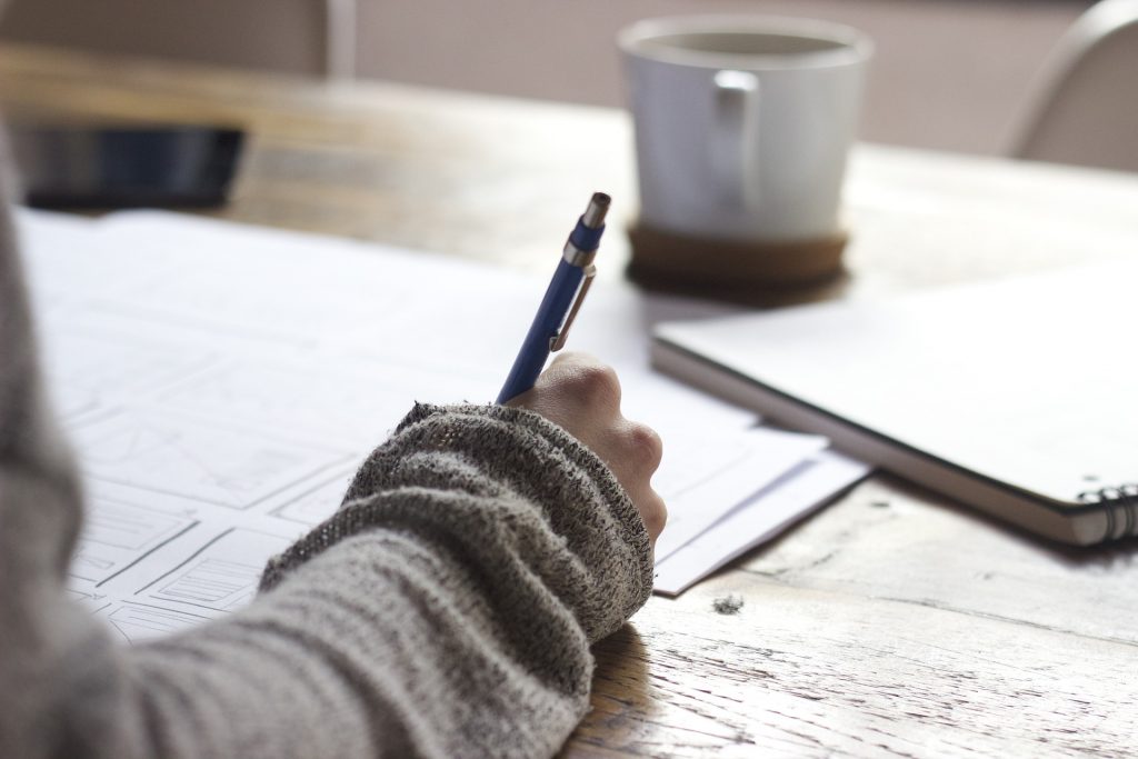 Someone writing on paper on a wood desk