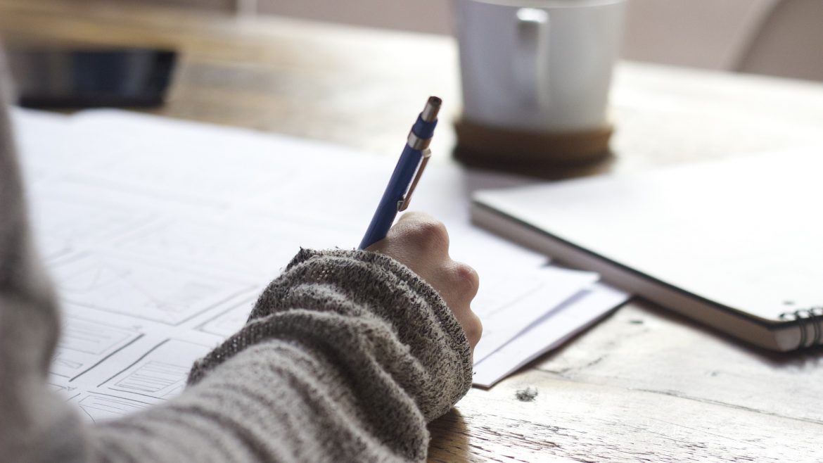 Someone writing on paper on a wood desk