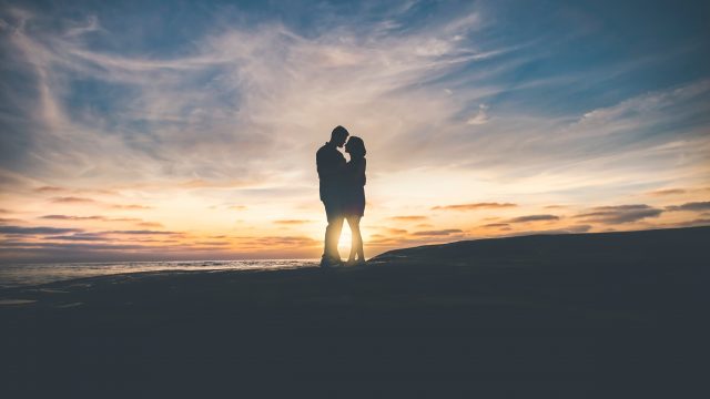 A man and a woman stand in silhouette against a sunset