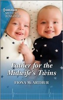 Two smiling twin babies look up at the viewer. They're wearing matching sleepers, one white with blue stars and one blue with white stars.