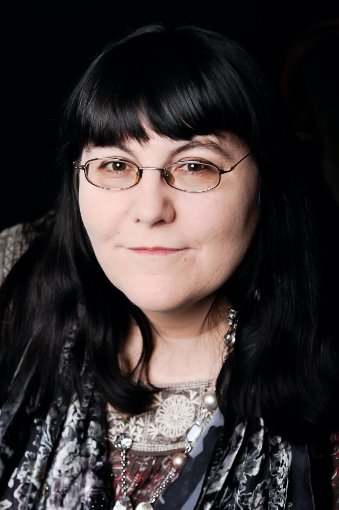 Close up of author Jane Holland. She has dark hair with bangs and she wears glasses.