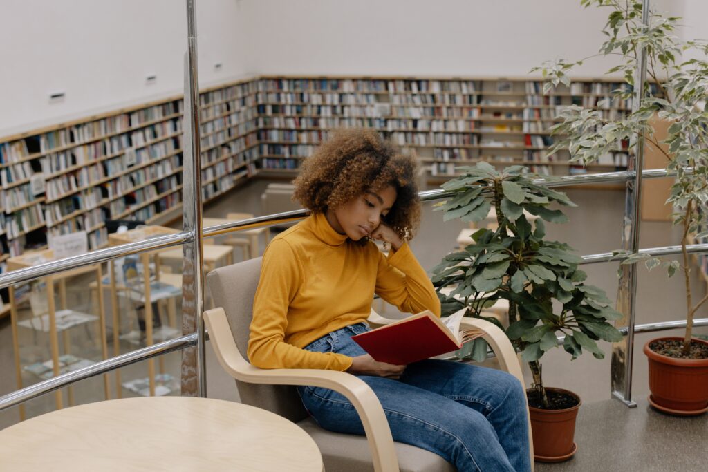 Young girl sitting in a library, reading a book.