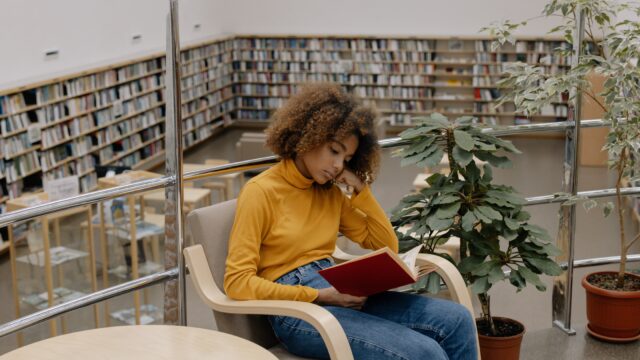 Young girl sitting in a library, reading a book.