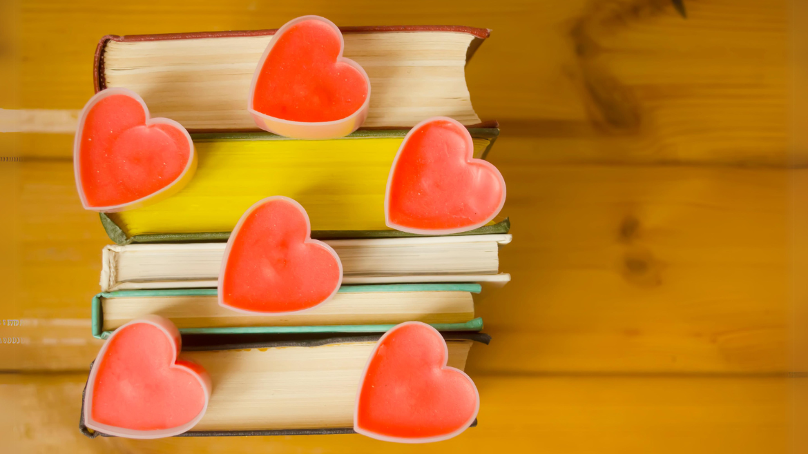 A pile of books on a wooden table. Red wax hearts sit on top of the books.