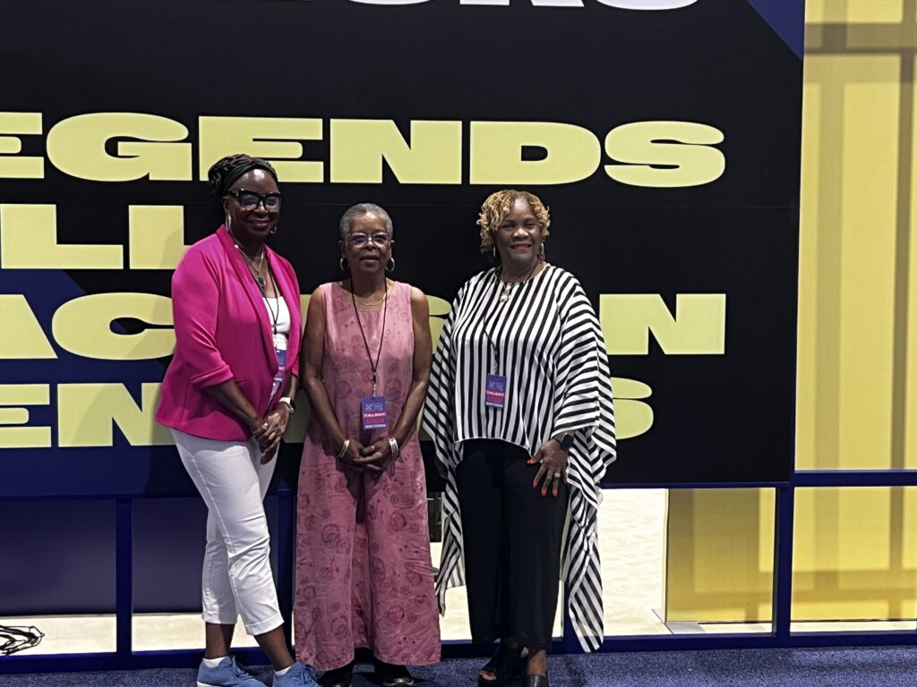 Harlequin authors Donna Hill, Beverly Jenkins, and Brenda Jackson stand on a black and yellow stage