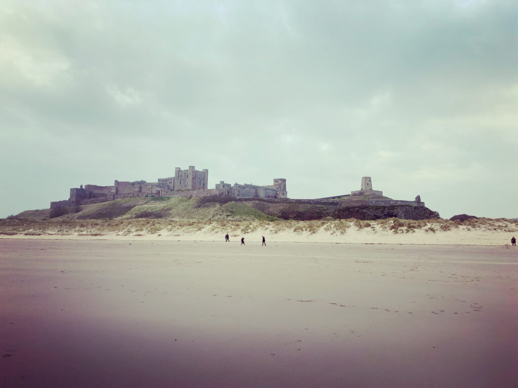 A large stone fortress sits overlooking a beach on a grey day