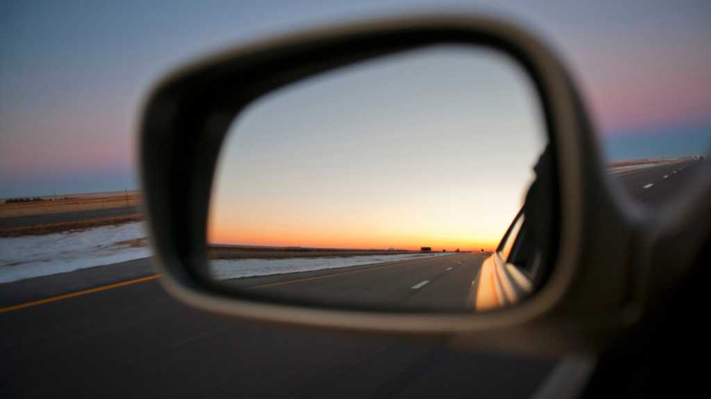 A photo of a rearview mirror of a car, looking back at the sunset