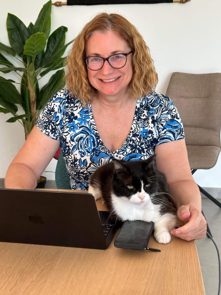 Author Michele Dunaway sits at a desk in a blue top with a cat tucked under her arm