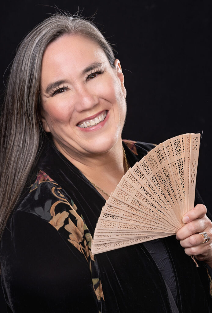 An author wearing a velvet jacket with long hair and holding an ornate fan.