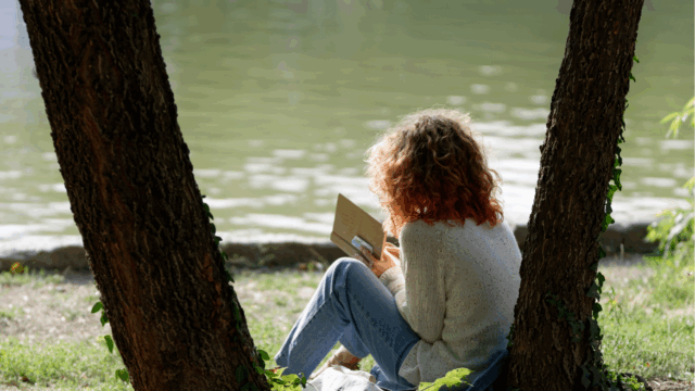 A woman reads a book under a tree