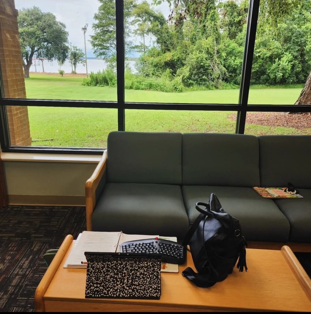 A bag and a keyboard sit on a table across from a large window onto a green field