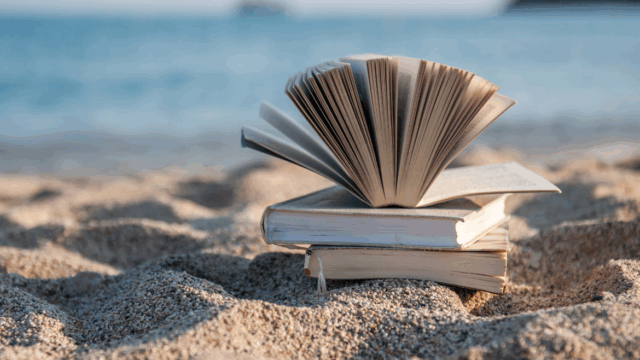 A stack of books sits on a sandy beach
