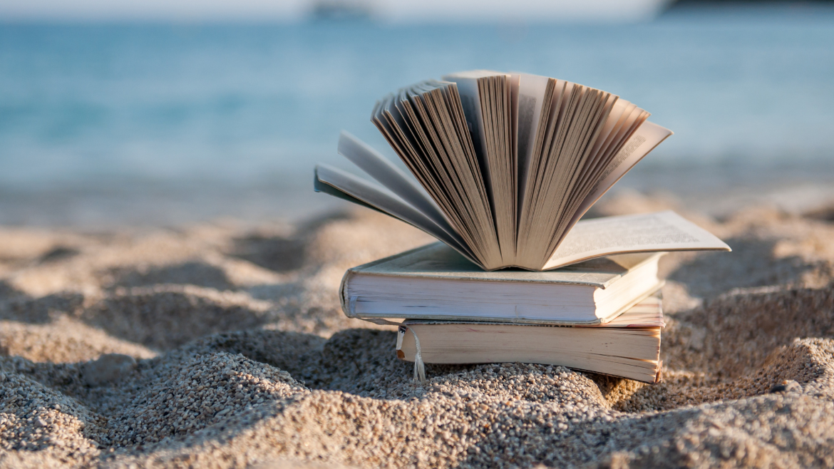 A stack of books sits on a sandy beach