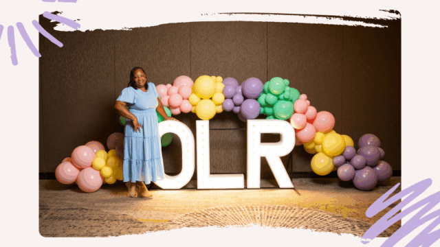 AC Arthur stands in a blue dress in front of a balloon arch reading OLR